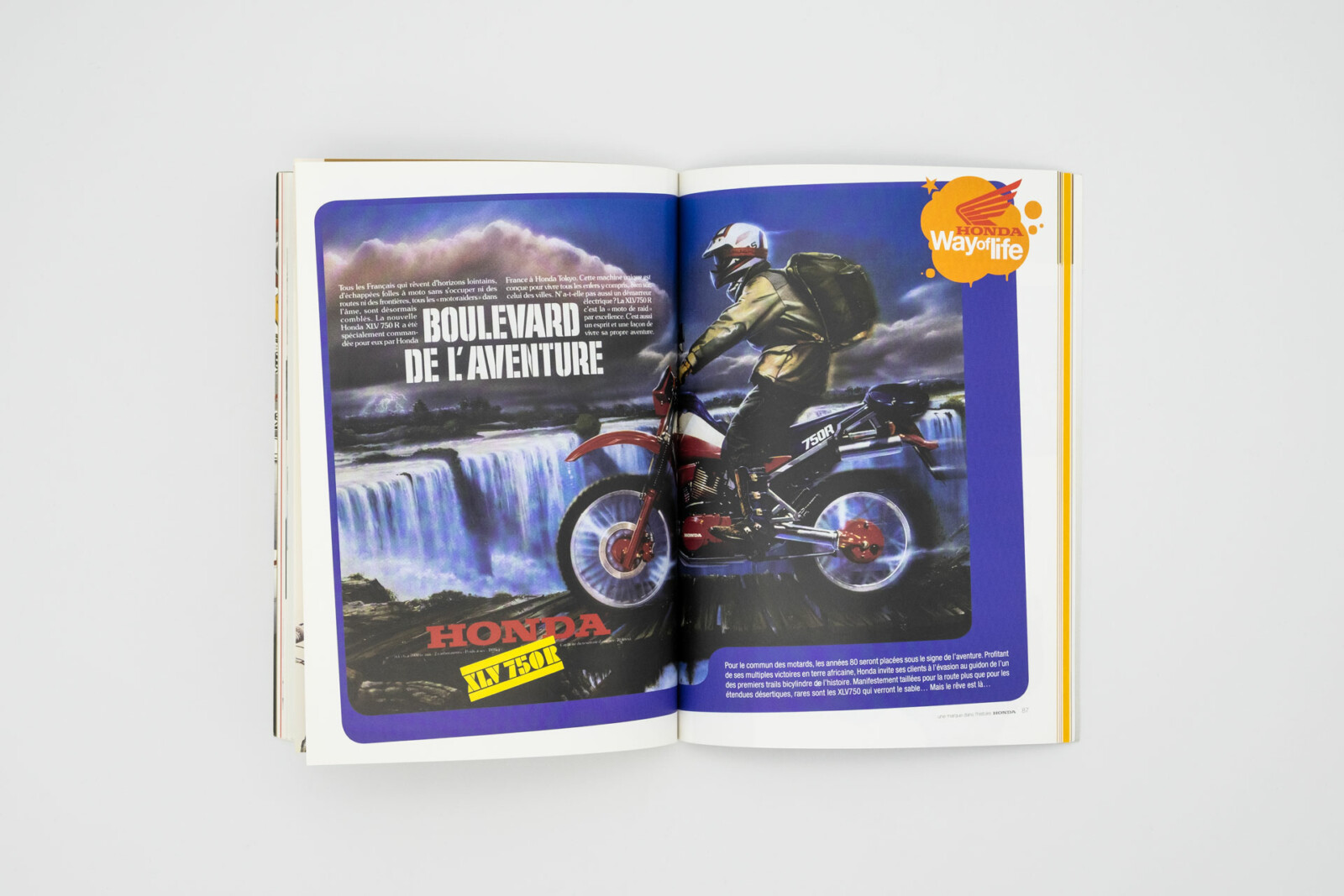 Vu du livre ouvert, double page figurant un motard sur une Honda XLV 750R, en fond, une chute d’eau.