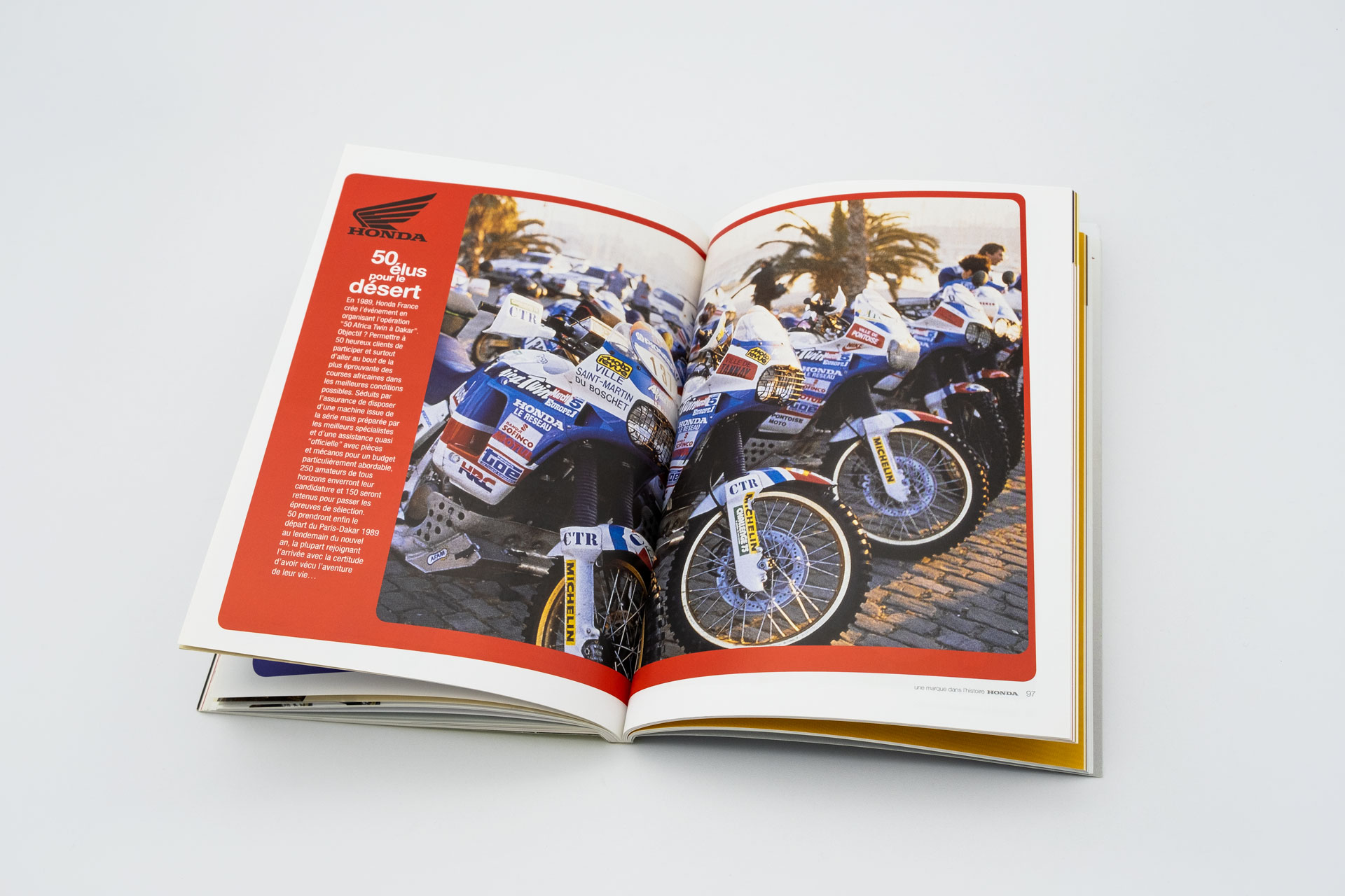 Vue du livre ouvert, une fine colonne de texte à gauche, une grande photo sur la double page montrant des motos de course alignées, sans pilotes. Vue du livre ouvert, une fine colonne de texte à gauche, une grande photo sur la double page montrant des motos de course alignées, sans pilotes. Vue du livre ouvert, une fine colonne de texte à gauche, une grande photo sur la double page montrant des motos de course alignées, sans pilote.