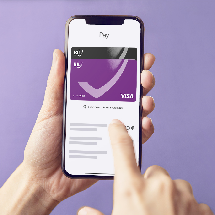 Vue zoomée sur les mains d’un détenteur de carte Visa émise par la BIL qui tiennent son smartphone. L’écran indique qu’un paiement sans contact est en cours.