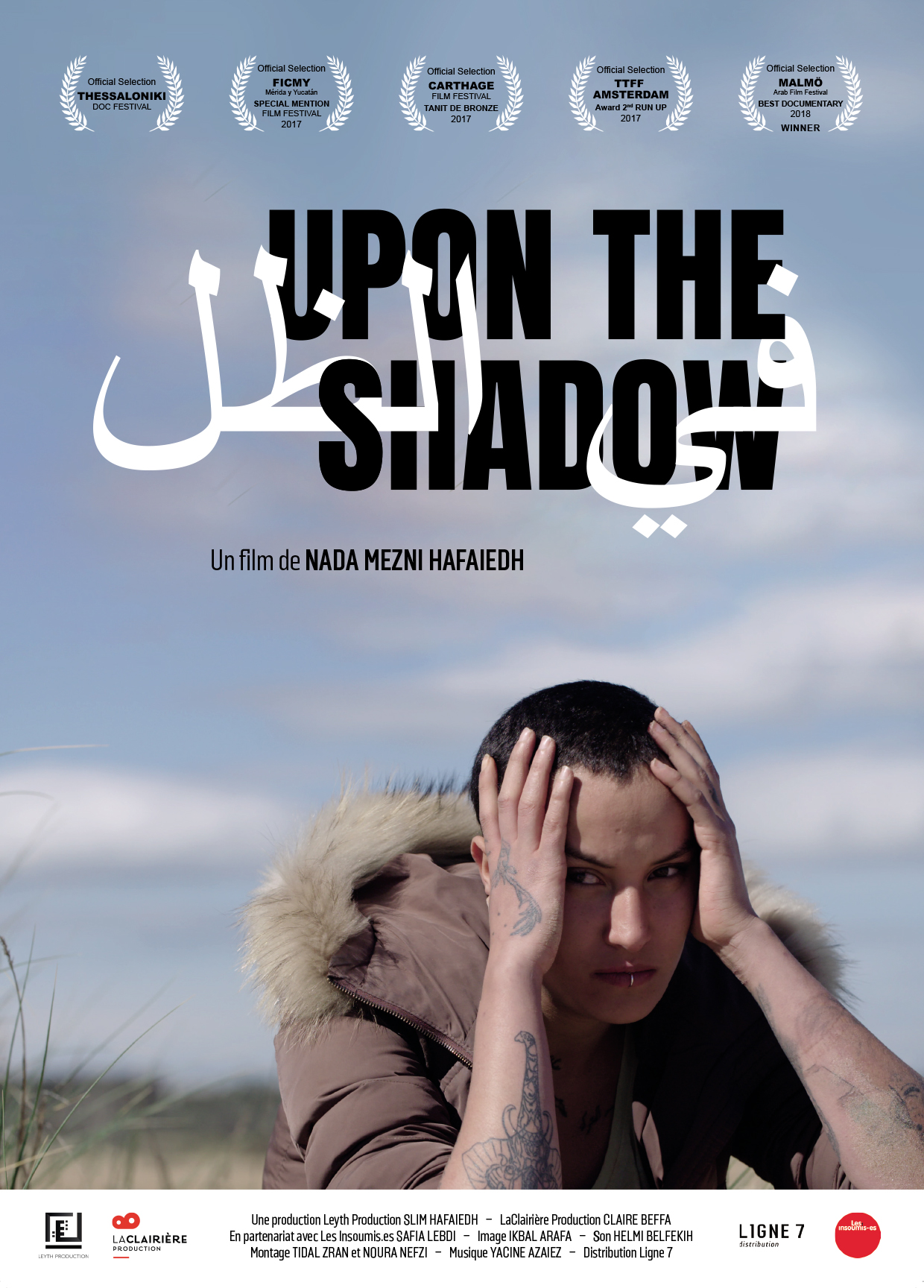 Affiche du film « Upon the shadow », une personne la tête dans ses mains est visible sous le titre en haut de casse noir, par-dessus en blanc, le titre en arabe.