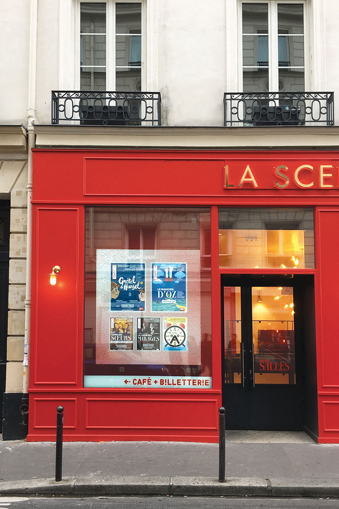 Vue tronquée de la façade rouge du théâtre, sous des balcons parisiens, la vitrine laisse voir les affiches des pièces et spectacles de la programmation.